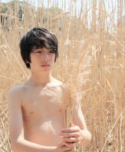 Shirtless boy standing against plant