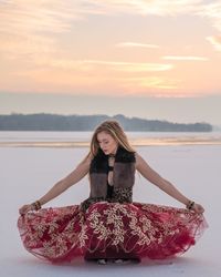Young woman in dress on snow covered field against sky during sunset