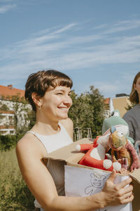 Happy female volunteer holding box with stuffed toys during charity drive at community center