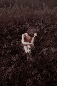 Rear view of woman sitting on field holding a mirror in front of her face