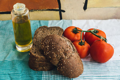 High angle view of brown bread with olive oil bottle and tomatoes on tablecloth at table