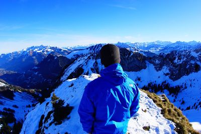 Rear view of man standing on snowcapped mountain against blue sky