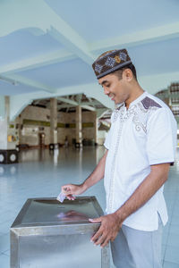 Smiling man donating money in box at mosque