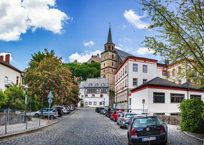 Street amidst trees and buildings against sky in city