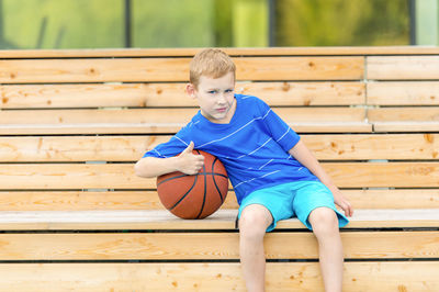 Portrait of boy gesturing and sitting by basketball on seat