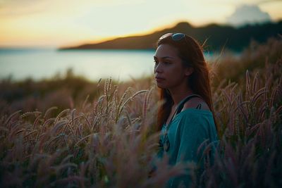 Young woman sitting on field against sky during sunset