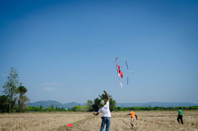 Rear view of man flying kite against blue sky