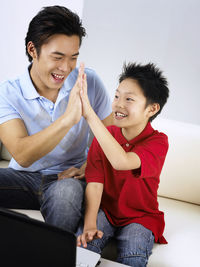 Happy father giving high-five to son while sitting on sofa