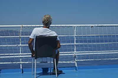 A man in a white shirt sits on the front deck of the ship looking out at the sea