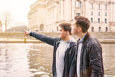 Young man with friend pointing at river in city