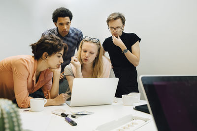Multi-ethnic colleagues planning strategy while looking at laptop in illuminated office board room