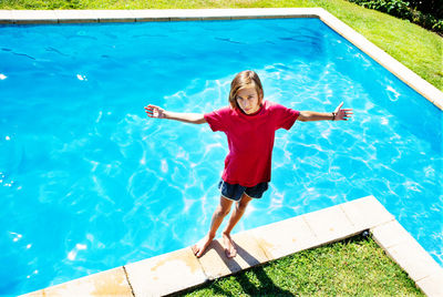 Boy with arms outstretched standing by pool