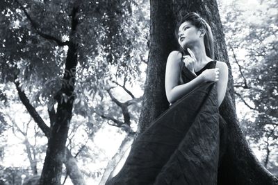 Low angle view of young woman standing against tree