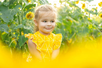 Happy little kid girl playing in blooming sunflower field on sunny summer day