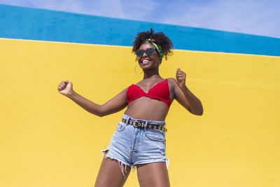 Smiling young woman dancing against yellow wall