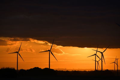 Silhouette wind turbines on field against sky during sunset