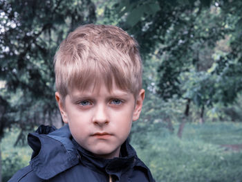 Portrait of boy wearing blue raincoat against trees