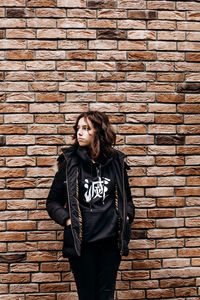 Portrait of teenager girl in front of bricks wall. black wearing teen looking aside