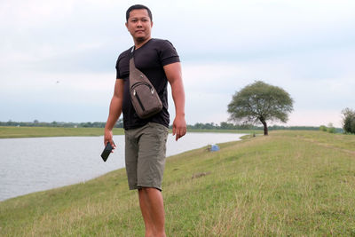 An indonesian young man standing on the field by the lake