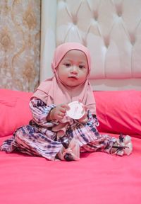 Portrait of cute baby girl sitting on bed at home