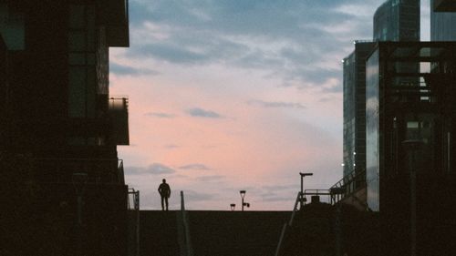 Silhouette people standing by street against sky during sunset