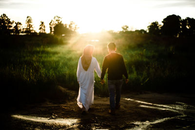 Rear view of friends walking on landscape against sky during sunset