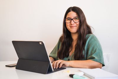 Young spanish brunette wearing glasses teleworking with her hybrid tablet laptop adapting her business to the new normal after the covid 19 global pandemic. she looks at camera and smiles