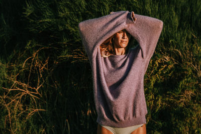 Midsection of woman wearing hat standing by tree looking to the camera and against the sun