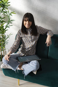 Smiling female professional with graphic tablet sitting on sofa at office