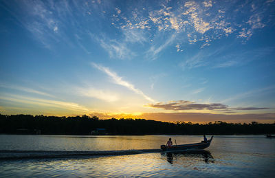 Silhouette people on boat in lake against sky during sunset