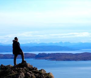 Rear view of man standing on rock against sky