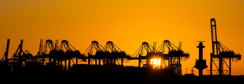 Silhouette cranes against clear sky during sunset