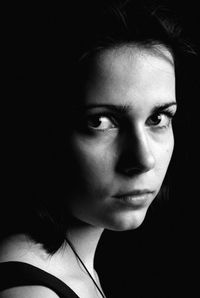 Close-up portrait of young woman standing on black background