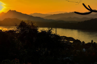 Scenic view of lake by silhouette mountains against orange sky
