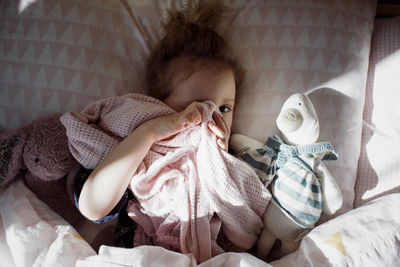 Overhead portrait of cute girl covering eye with textile while lying on bed at home