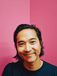 Portrait of smiling young man against pink wall