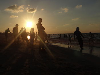 Silhouette people at beach against sky during sunset