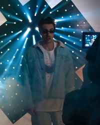 Young man standing by illuminated lights at night