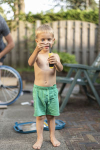 Full length of shirtless boy holding tool while standing outdoors