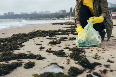 Environmentalist collecting garbage in garbage bag while crouching at beach