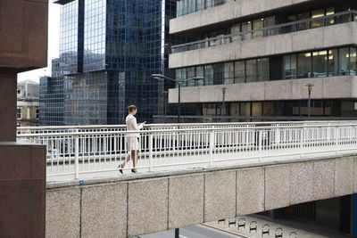 Businesswoman using smart phone while walking on footbridge at downtown district