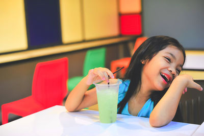 High angle view of happy girl drinking juice while sitting in restaurant