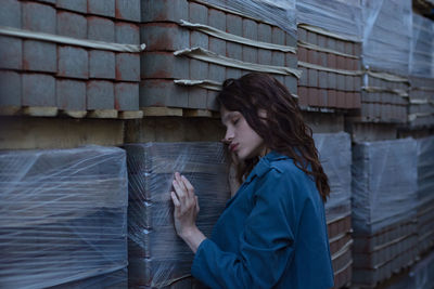 Side view of woman standing against stacked bricks