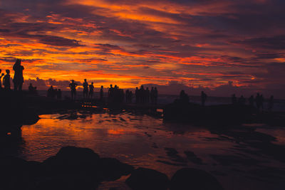 Silhouette people on beach against orange sky