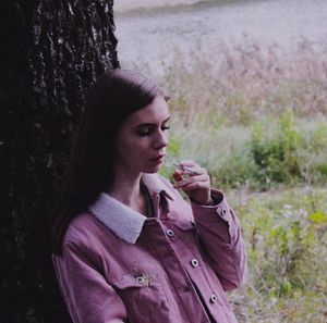 Young woman smoking cigarette by tree on field