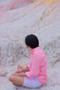 Rear view of woman sitting against pink wall