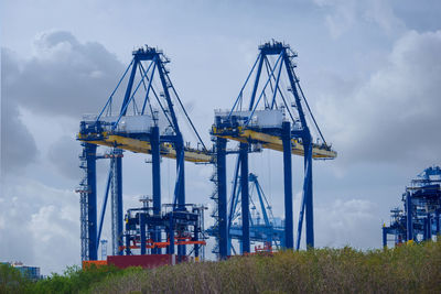 Cranes at harbor against sky