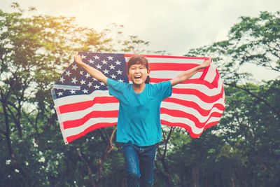 Happy teenage girl with american flag against trees