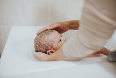 Close-up of father holding baby girl in bathtub at bathroom