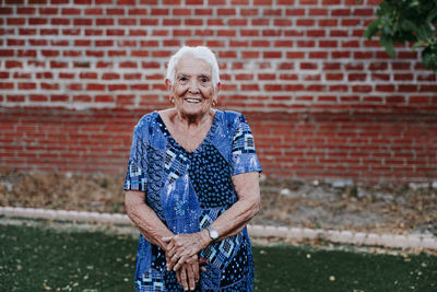 Portrait of smiling senior woman standing against brick wall